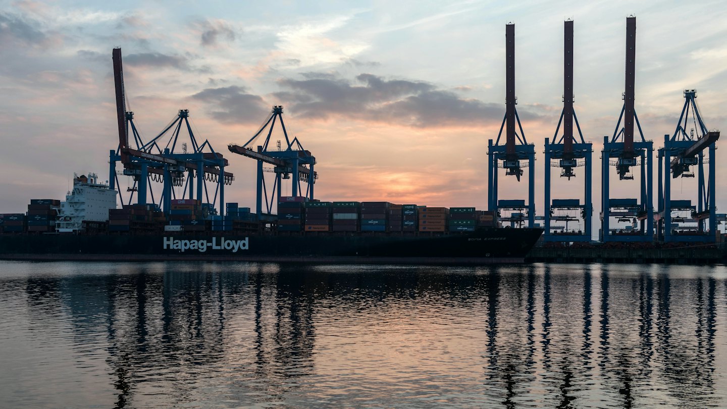Container ship docked at port with cranes at sunset.