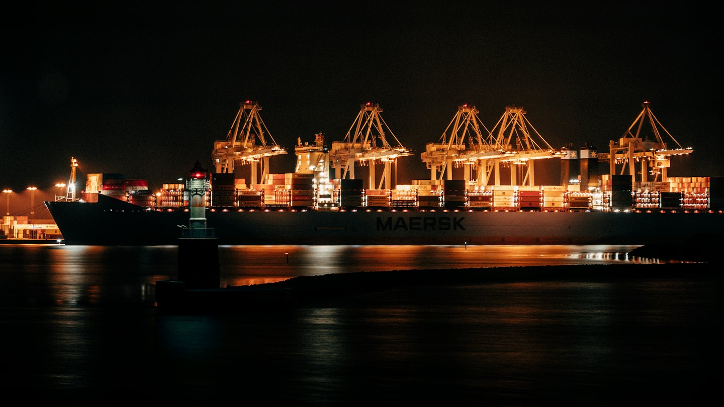 Cargo ship loaded with containers at a busy port at night.
