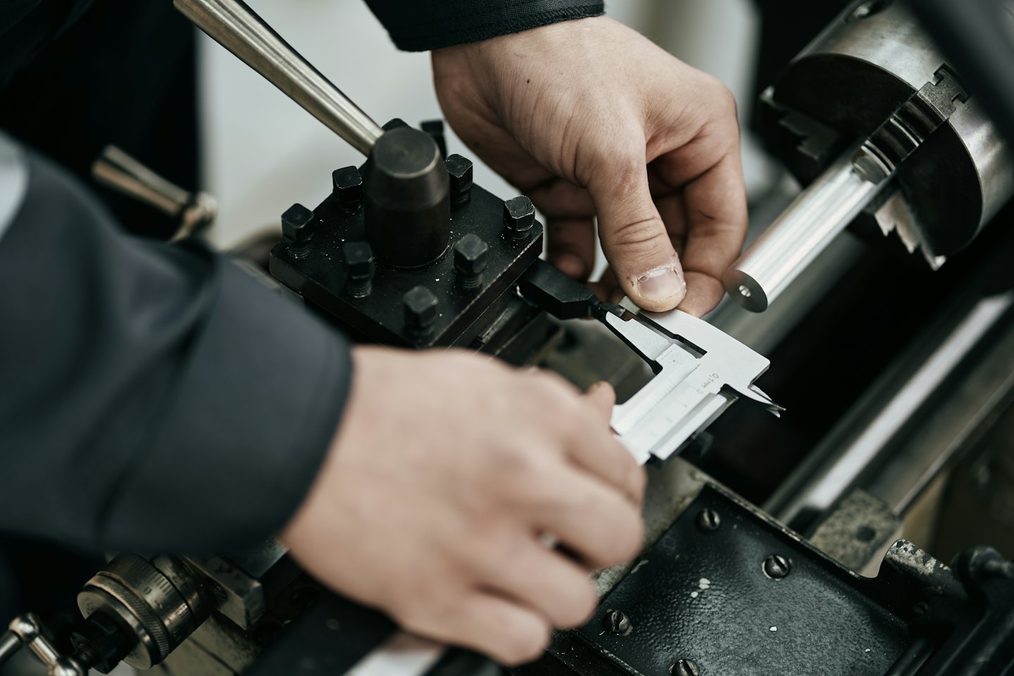 Hands measure metal part with calipers in lathe machine.