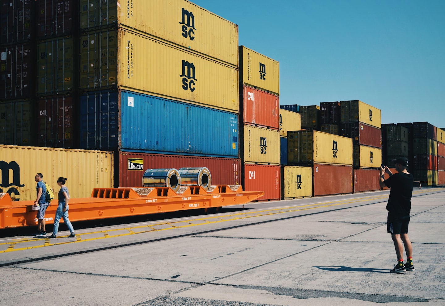 Man photographs stacked colorful shipping containers at a logistics facility.